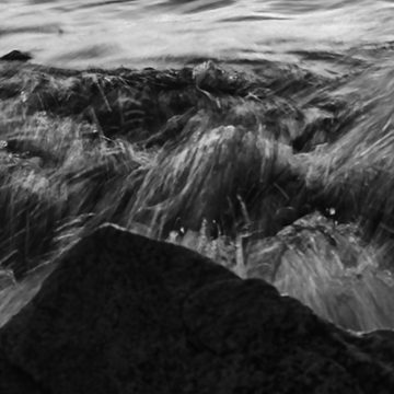 Fragmento de la fotografía de una pequeña ola golpeando contra una piedra al atardecer